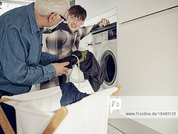 Enkel und Großvater legen zu Hause Wäsche in die Waschmaschine