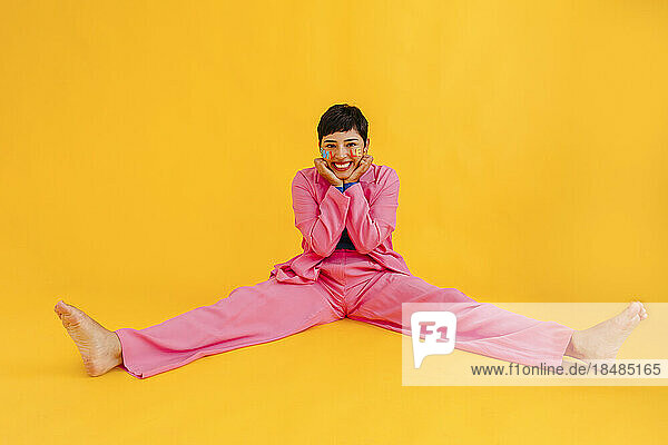 Happy young woman sitting with legs apart in over yellow background