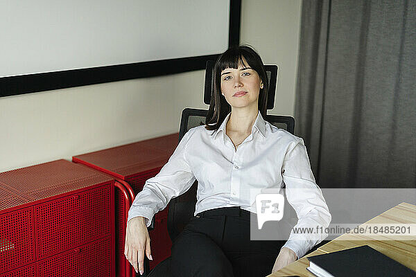 Porträt einer selbstbewussten brünetten Geschäftsfrau  die im Büro am Schreibtisch sitzt