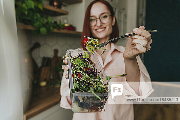 Woman showing fresh salad in kitchen at home
