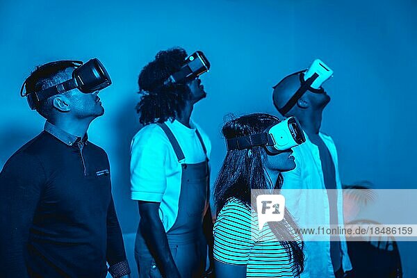 Gruppe junger Menschen mit VR Brille in einem Virtual Reality Spiel in einem blauen Licht  futuristisch oder Wissenschaft  Technologiekonzept Blick nach rechts