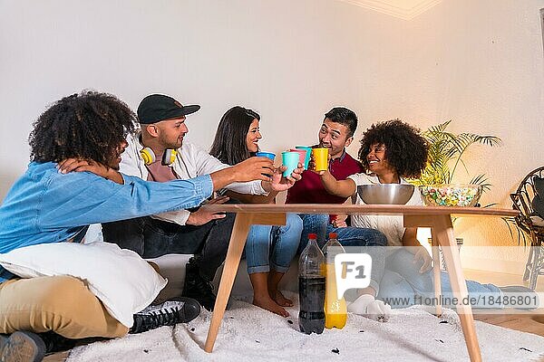 Eine Gruppe von Freunden isst Popcorn und stößt mit Softdrinks an. Lachen beim Anschauen eines lustigen Films im Fernsehen zu Hause