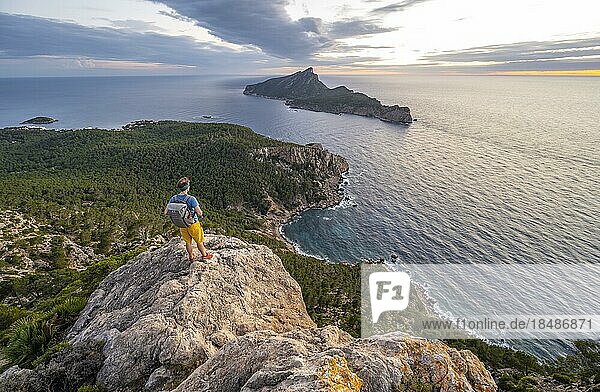Ausblick auf Berge und Küste mit Meer  bei Sonnenuntergang  Wanderer auf einem Felsen  Wanderung nach La Trapa von Sant Elm  hinten Insel Sa Dragonera  Serra de Tramuntana  Mallorca  Spanien  Europa