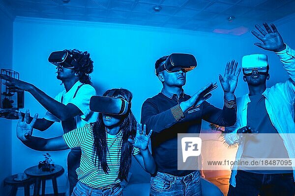 Gruppe junger Menschen mit VR Brille in einem Virtual Reality Spiel in einem blauen Licht  erstaunt berühren virtuelle Objekte  futuristisch oder Wissenschaft  Technologiekonzept