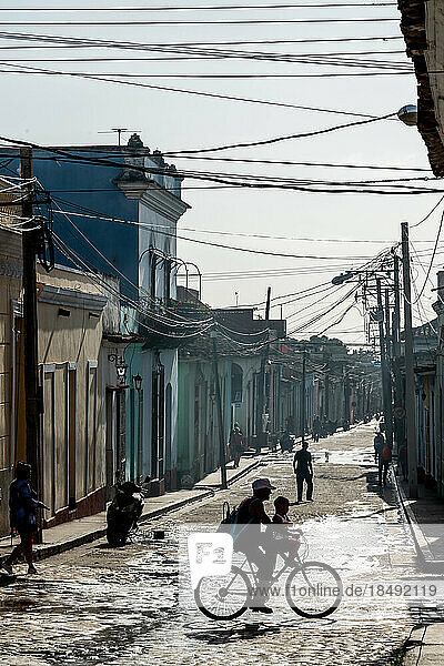 Typische Seitenstraße unter einem Gewirr von Telefonkabeln  Silhouette einer Familie auf einem Fahrrad  Trinidad  Kuba  Westindien  Karibik  Mittelamerika