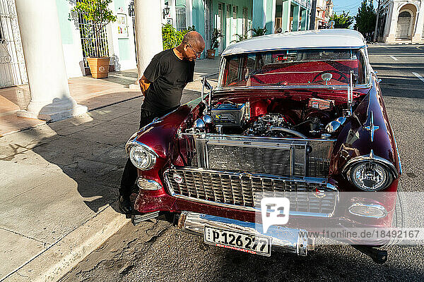 Kubanischer Mann inspiziert und bewundert den offenen Motor eines roten Chevrolet-Klassikers  Cienfuegos  Kuba  Westindien  Karibik  Mittelamerika