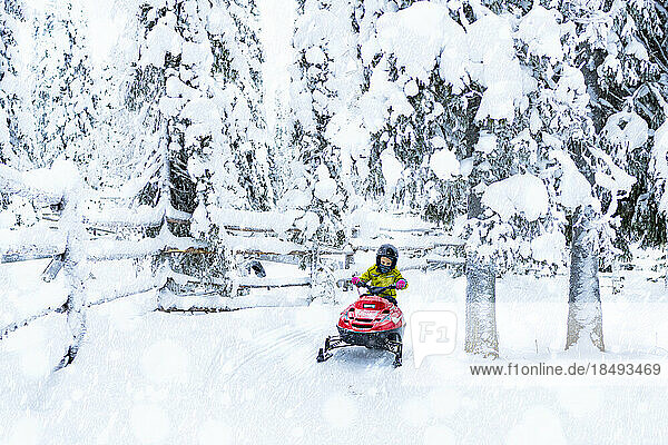 Glücklicher Junge  der ein Schneemobil in den arktischen Wäldern fährt  Lappland  Finnland  Europa