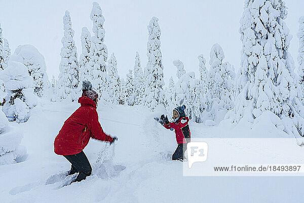 Fröhliche Mutter und Sohn genießen das Spiel mit dem Schnee in der Winterlandschaft von Finnisch-Lappland  Finnland  Europa