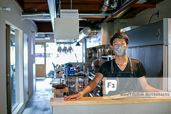 A man in a face mask at the counter of a restaurant kitchen  the owner or manager.