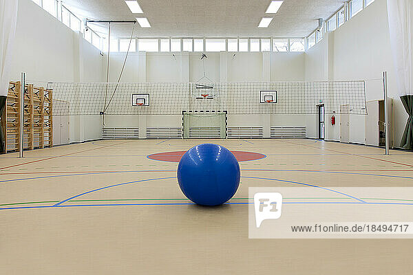 Sports facilities in a high school  a large gym with sports courts  basketball hoops and a goal  a blue ball.