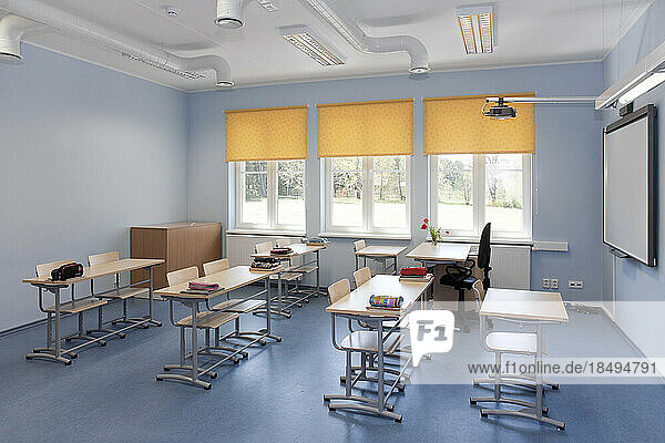 A school classroom with desks and chairs and yellow window blinds.