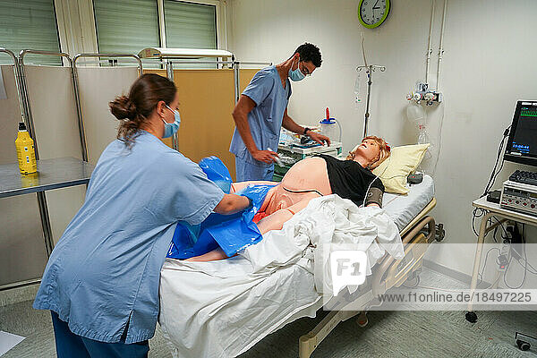 Students facing a post natal emergency follow procedures on a mannequin. This dummy is controlled by operators in an adjoining room. Here  a woman with heavy bleeding following a home birth. Intervention of a student in intensive care.