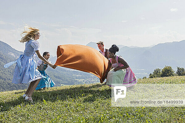 Teenage friends spreading picnic blanket on grass landscape  Bavaria  Germany