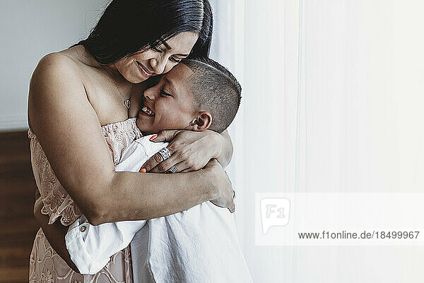 Side view of mother and young son hugging in natural light studio