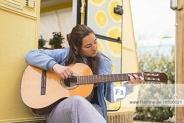 Young woman playing guitar at a campsite.
