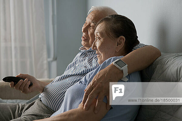 Senior couple watching tv and using remote control at home