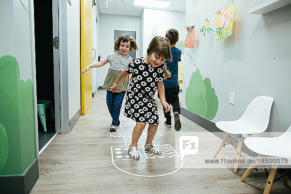 Girls hopscotch together inside an educational facility