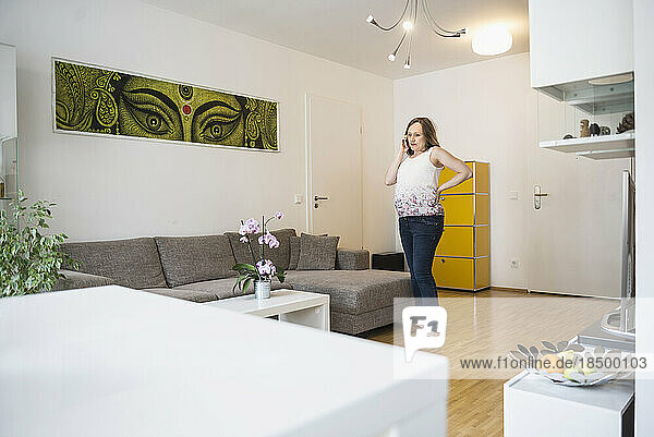 Pregnant woman standing in living room and talking on mobile phone  Munich  Bavaria  Germany