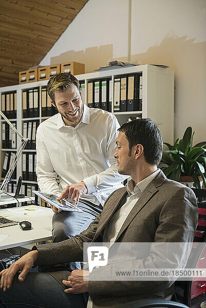 Two businessmen using digital tablet in an office and smiling  Bavaria  Germany