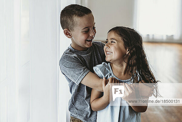 Brother and sister laughing at each other in natural-light studio