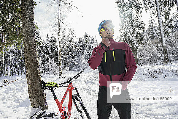 Young biker wearing zipper jacket by bicycle in snow