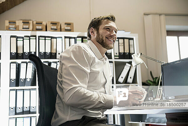 Mid adult businessman drinking coffee in an office and smiling  Bavaria  Germany