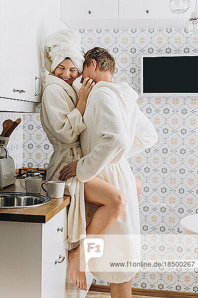 A couple in white terry bathrobes hugging in the kitchen