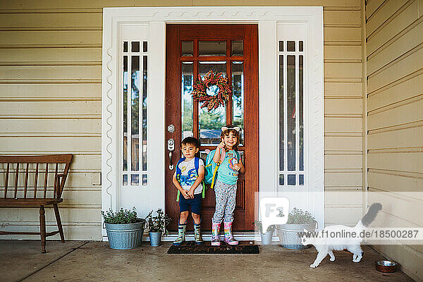 Young boy and girl standing outside front door wearing back packs