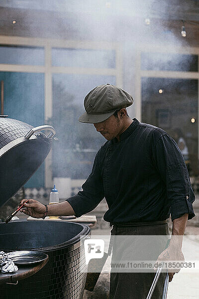 Asian man in uniform cooks on the grill outdoors. Kitchen staff