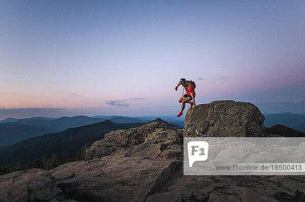 Trail runner man leaping off rock on top of mountain at sunrise