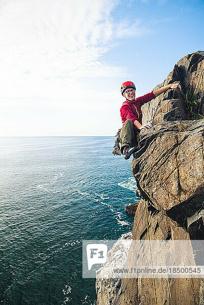 Woman wearing red trad climbing on lead with ocean below