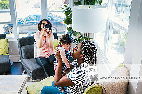 Lesbian photographing playful girlfriend and baby boy in living room at home