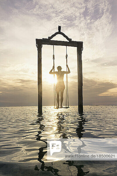 Young man standing on rope swing at beach against sunset  Gili Trawangan  Lombok  Indonesia