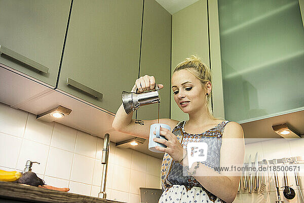 Beautiful young woman pouring coffee in the kitchen  Munich  Bavaria  Germany