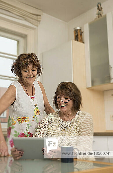 Two senior roommates using a digital tablet and smiling in the kitchen  Munich  Bavaria  Germany