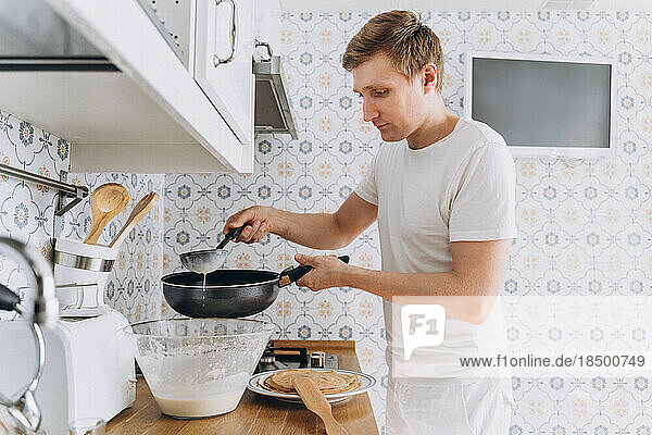 Young man in white having funcooks pancakes