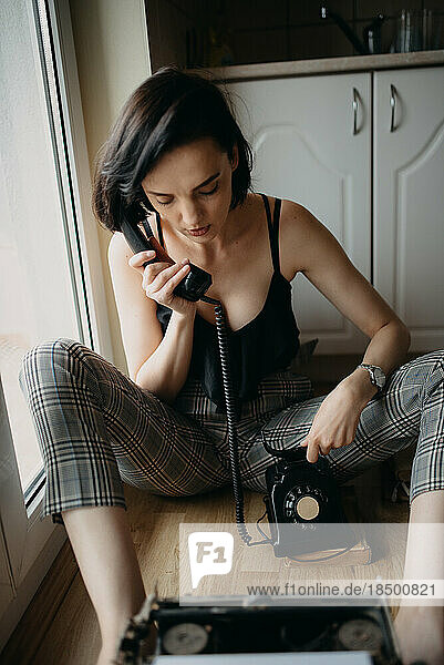 Woman in plaid pants sitting on the floor talking on the phone.