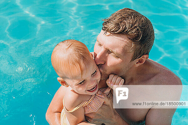 A man kisses his little daughter on the cheek in the open pool