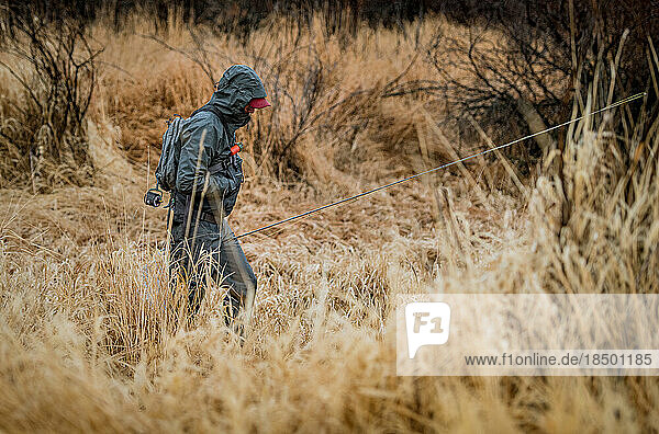 Fly fisherman in waterproof clothing walking through field