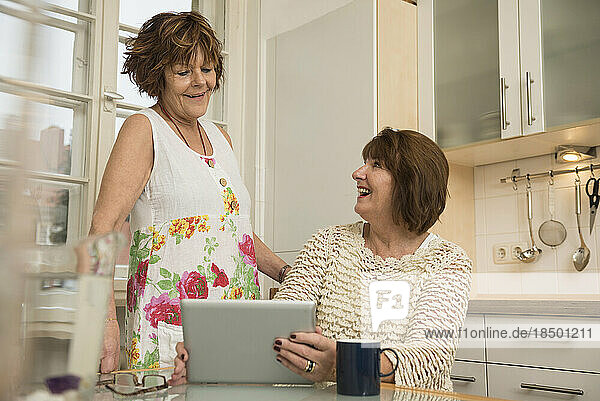 Two senior roommates using a digital tablet and smiling in the kitchen  Munich  Bavaria  Germany