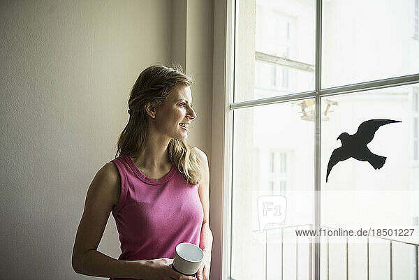 Young woman looking through window and having coffee  Munich  Bavaria  Germany