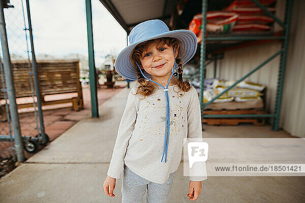 Young girl smiling wearing sun hat outside of garden center