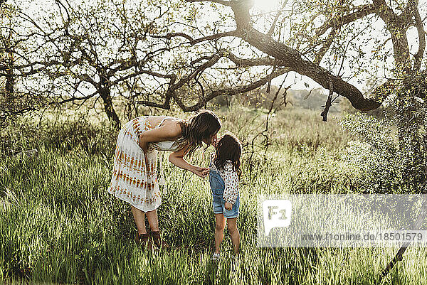 Side view of mother bending down to kiss daughter in backlit field