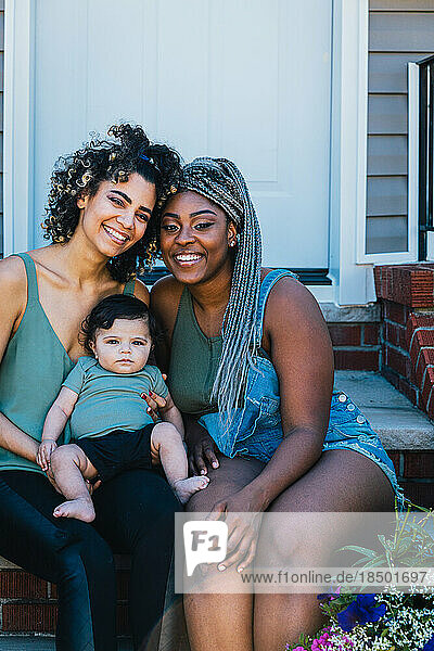 Portrait of happy lesbian mothers and cute son sitting outside house