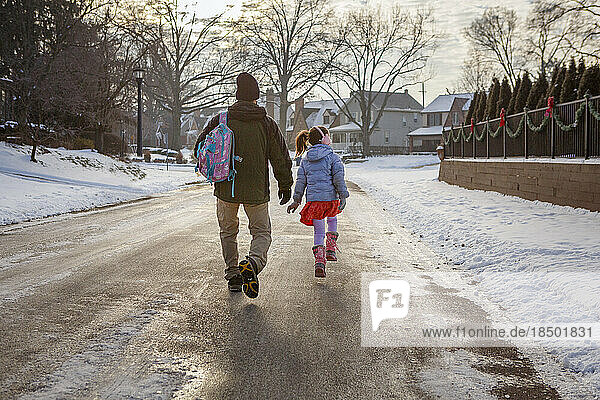 Rear-view of father and daughter walking to school on snowy street