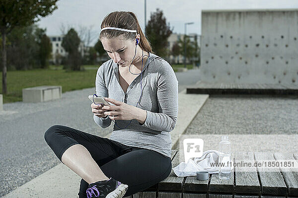 Young woman taking a break after exercising and checking sports test results on mobile phone  Bavaria  Germany