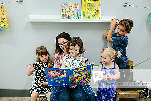 Teacher and four students read a book together