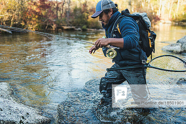 A fly-fisherman wading through a stream in late season