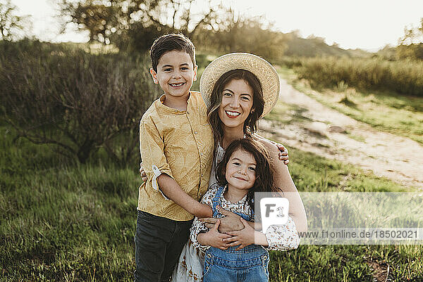 Portrait of happy young mother and children smiling in backlit meadow