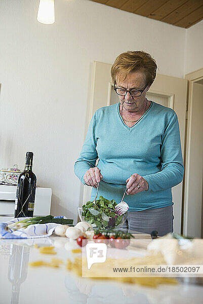 Old woman mixing salad on the kitchen table